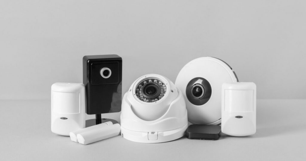 White CCTV dome camera with black lens, surrounded by motion detectors and security accessories on a gray background.